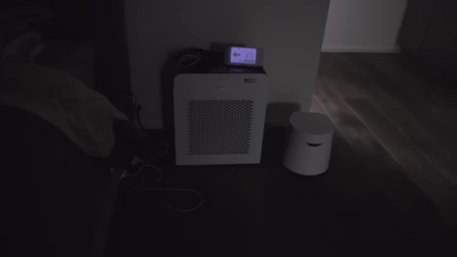 Two air purifiers and an air quality monitor are visible in a darkened bedroom, emphasizing comprehensive air quality control.