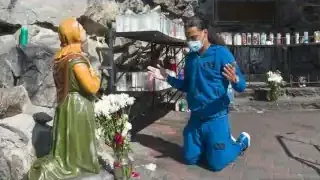 A person praying at an outdoor grotto shrine resembling Lourdes, with bottles of water, an example of how people create and utilize sacred spaces.