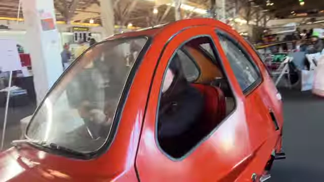 A small, red, bubble-shaped car on display in the motor-based exhibits area.