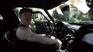 A father sits in his newly gifted 1967 Corvette, smiling widely.
