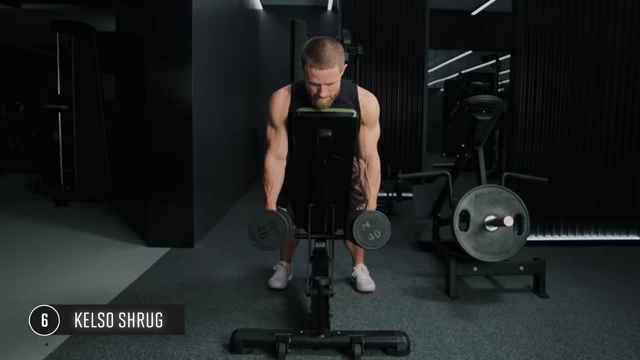 Man performing Kelso shrugs using dumbbells while bracing against an incline bench