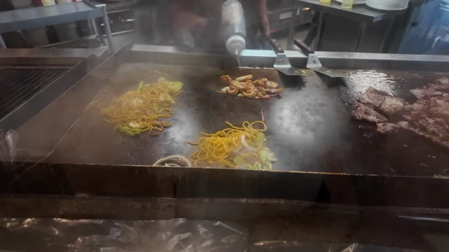 Chefs cooking chow mein and meats on the Teppanyaki grill.