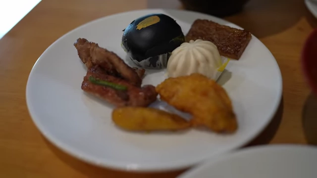 A plate with dim sum items like steamed buns, plantain, and short ribs.