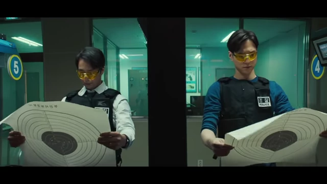 Two police officers hold up paper targets at a shooting range, revealing the anticlimactic reality behind the film's misleading opening gunshot.