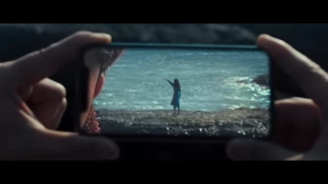 Hae-jun's phone screen displays Seo-rae standing by the ocean, symbolizing his distant and mediated observation of her.