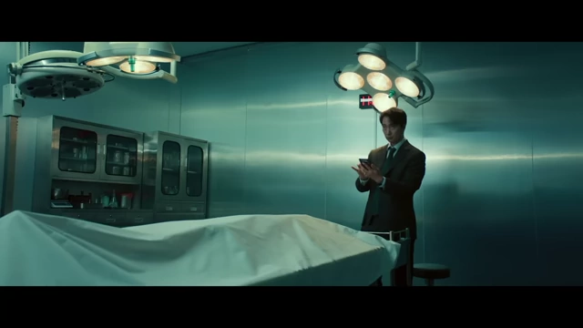 Hae-jun stands in a morgue, with the camera tilting upward, visualizing his mountain-like nature and desire for resolution.