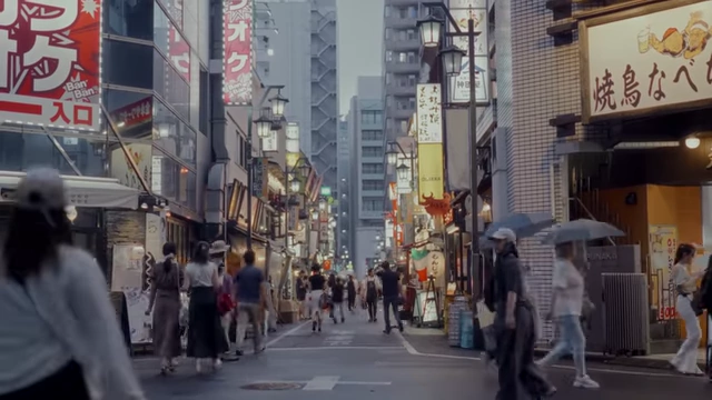 People walk on a busy street lined with shops and signs, representing a common urban scene.