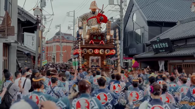 A traditional Japanese festival float is pulled through a town by a large crowd of participants.