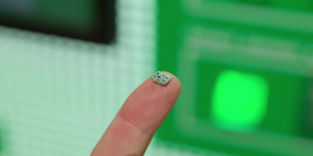 A tiny 1mm squared accelerometer rests on a fingertip, demonstrating its minuscule size.