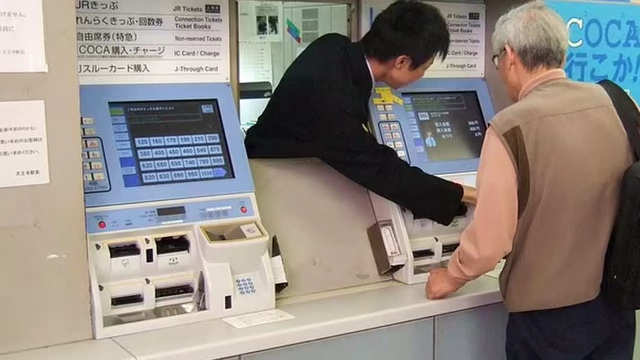 Station staff assisting a passenger at a ticket machine.