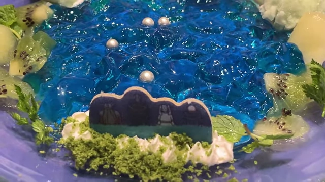 A blue jelly dessert with kiwi slices and silver balls, recreating a meteor shower, with a character cutout.