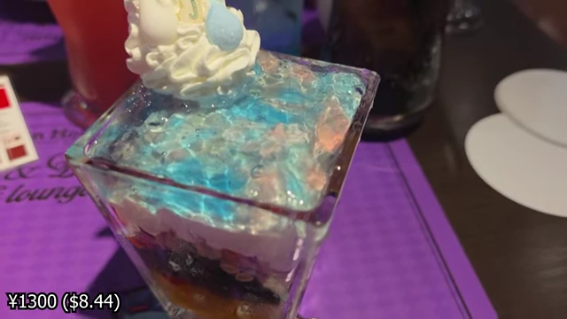 A tall glass filled with layered colorful jellies, fruit, and cream, with a character cutout on top.