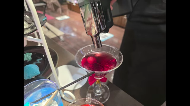 A staff member using a device to create a smoke bubble over a red drink in a martini glass.