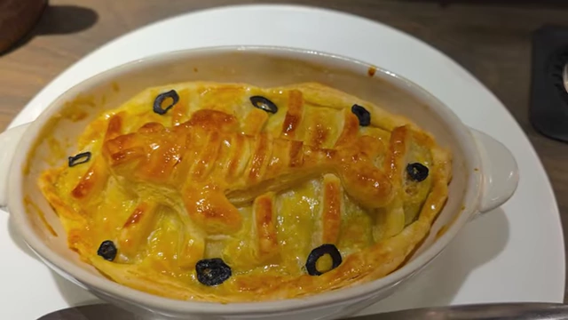 A fish-shaped baked pie in a white dish, garnished with olives.