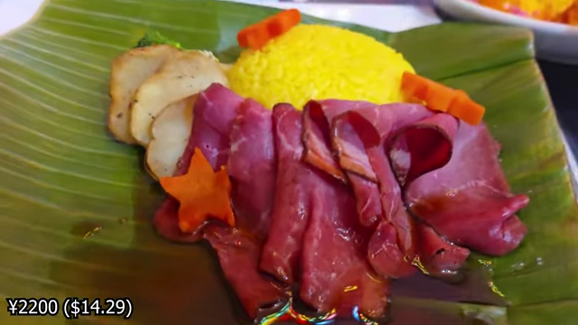 A British Sunday roast-inspired dish with sliced beef, saffron rice, potatoes, and carrots, served on a banana leaf.