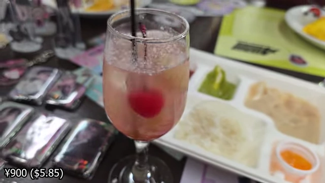 A pink lychee drink with ice and a cherry, served in a wine glass.