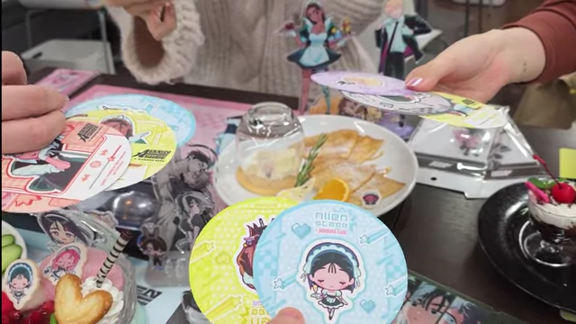 Hands holding several round coasters with different Alien Stage character designs.