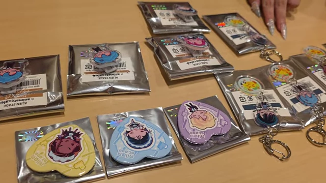 Various Alien Stage acrylic keychains and badges displayed on a table.