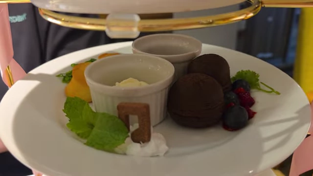 A close-up of the middle tier of an afternoon tea set, displaying chocolate desserts, a musical note cookie, and berries.