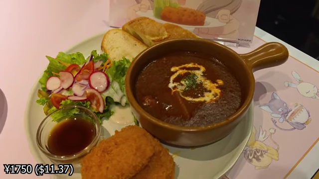 A dish containing beef stew, croquettes, a side salad, and bread slices, with a character cutout behind it.