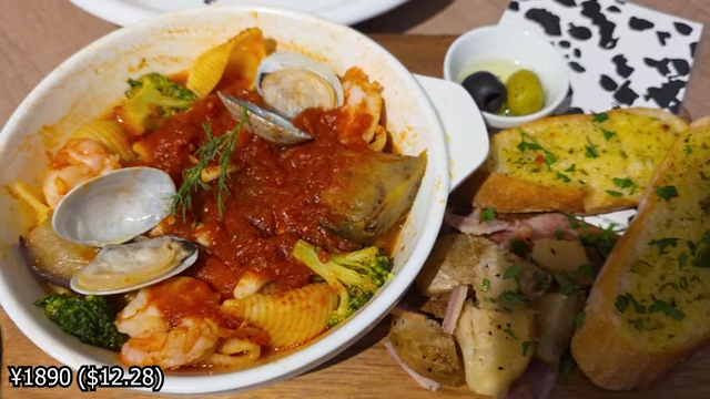 A bowl of tomato stew pasta with seafood like clams and shrimp, broccoli, and bread.