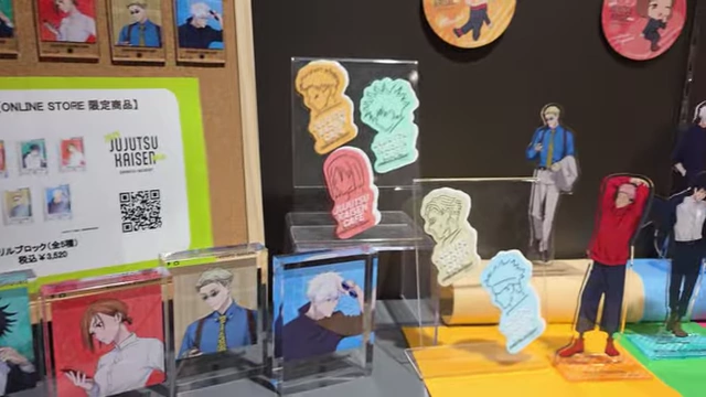 A display of Jujutsu Kaisen merchandise, including acrylic stands, badges, and stickers featuring chibi art.