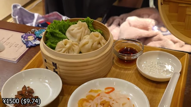 A dim sum steamer basket with three dumplings, served with pickled vegetables and sauces.