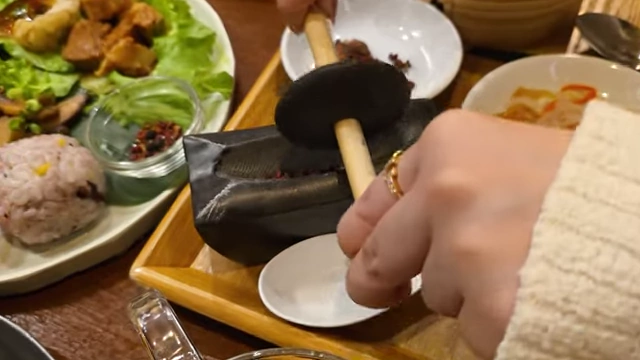 A hand operating a manual spice grinder over a small dish of spices.
