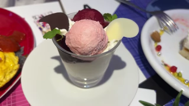 A mini parfait with two scoops of fruit sorbet over cream and granola, decorated with chocolate pieces.