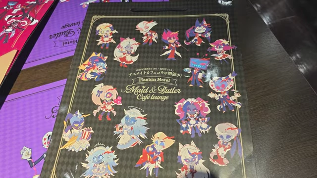 A large paper bag with Hazbin Hotel chibi character art on one side.