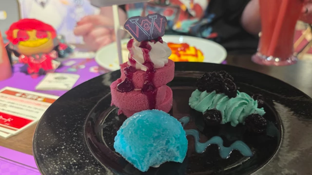 The bottom tier of a Hazbin Hotel-themed afternoon tea set, featuring a roll cake, ice cream, and mint cream with berries.
