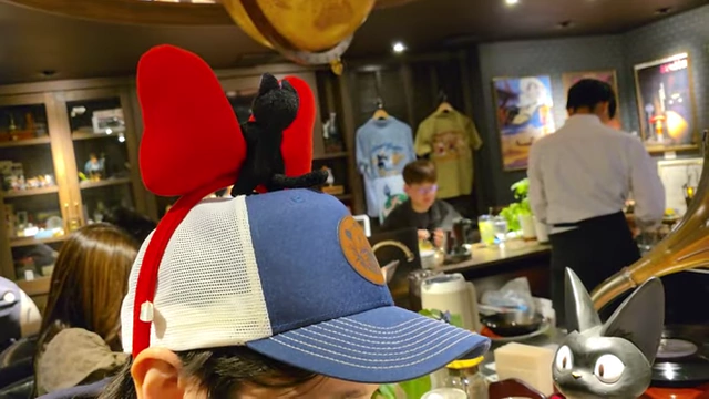 A person wearing a Kiki's Delivery Service headband with a red bow and Jiji the cat.