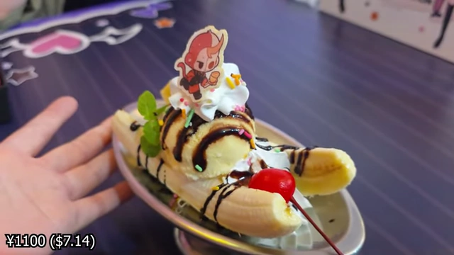 A banana split dessert with sliced bananas, ice cream, whipped cream, chocolate sauce, and a small character cutout on top.