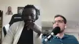 A man with glasses and a microphone speaks, gesturing with his hands, while discussing his PhD experience.