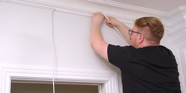 A close-up of thin cable channels being installed along the wall to hide speaker wires