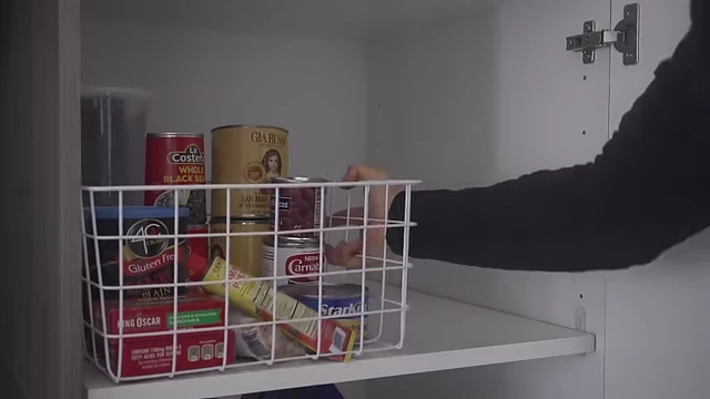 A shelf with a white wire bin containing canned goods