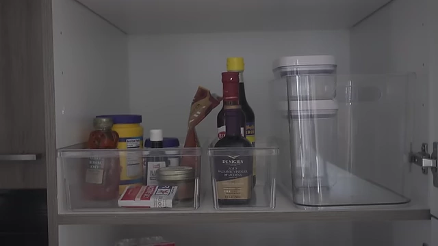 An organized pantry shelf with clear bins for baking items, vinegars, and pop containers for flour and rice