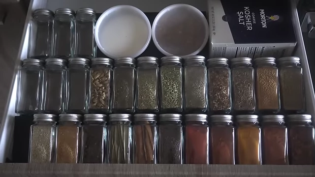 An organized spice drawer with uniform bottles and a salt container