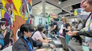The artist signing a book for a fan at a convention.