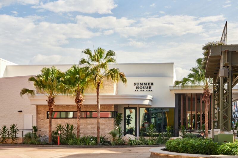 exterior shot of the restaurant, a white building with brick, palm trees and tropical landscaping.