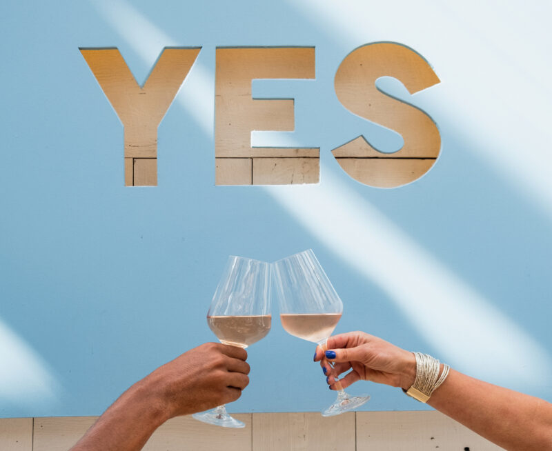 Two glasses of rosé cheersing in front of Summer House's blue sign that says