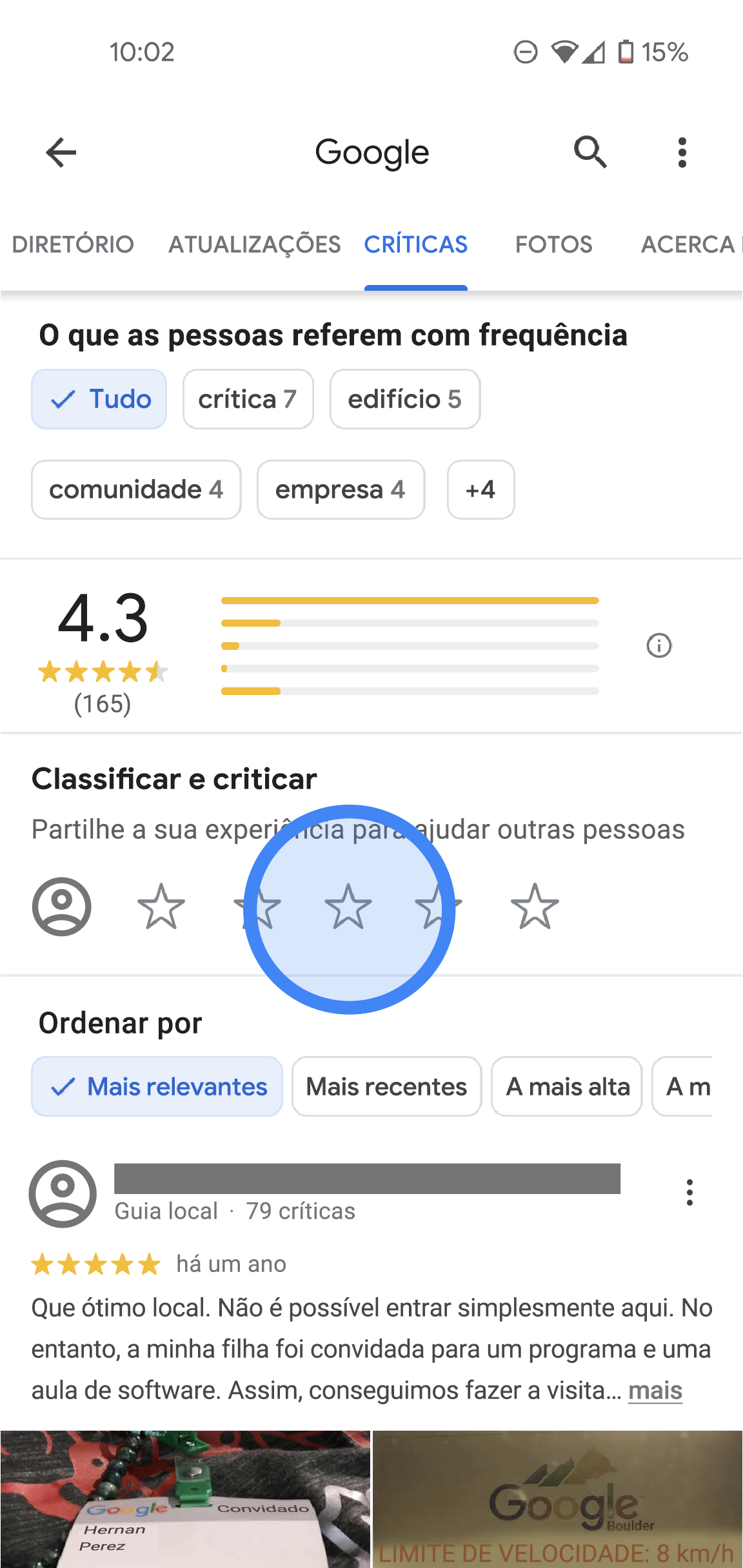 Na app Google Maps, é apresentado o separador Críticas da localização de um escritório da Google. Na parte superior, existem separadores com as etiquetas Diretório, Críticas, Fotos e Sobre. Abaixo, encontra detalhes das críticas, como a classificação média, a distribuição das classificações e uma lista de todas as críticas. No centro do ecrã, existe a secção "Classificar e criticar" que mostra 5 estrelas em branco. 