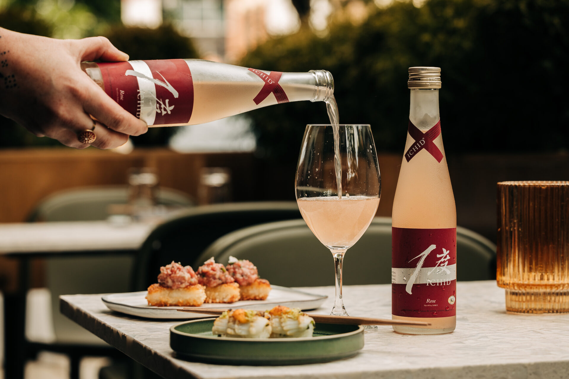 Hand pouring a bottle of sake into a wine glass with Tuna Crispy Rice in the background and another bottle of sake on the table