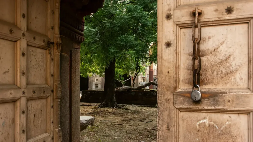 Old wooden doors left open to a courtyard, with a chain and padlock hanging unused on one side
