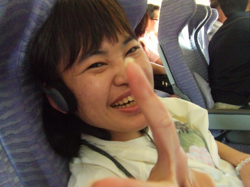 飛行機にのってとびきりの笑顔のMさんが、ピースをしている