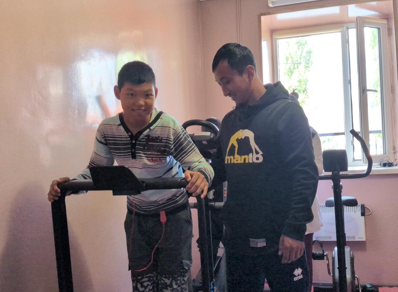 トレーニング器具を使用し笑顔を見せる子どもと施設のスタッフ
