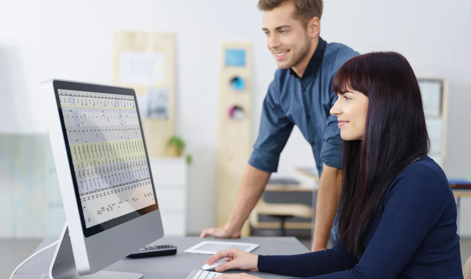 Due colleghi sorridenti collaborano su un foglio di calcolo al computer in ufficio.