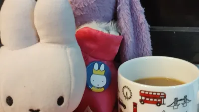 Miffy, a bunny wearing an orange top, is sitting in front of a purple bunny wearing a crown and a badge featuring Miffy in a crown, and next to a mug featuring the sights of London and Miffy in a crown.