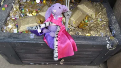 A purple bunny wearing a crown and a royal coat, sitting atop a big chest of gold, coins and gems.