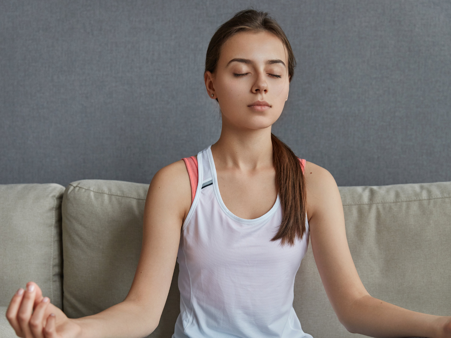 Žena u bijelom topu meditira na kauču fokusirana na disanje
